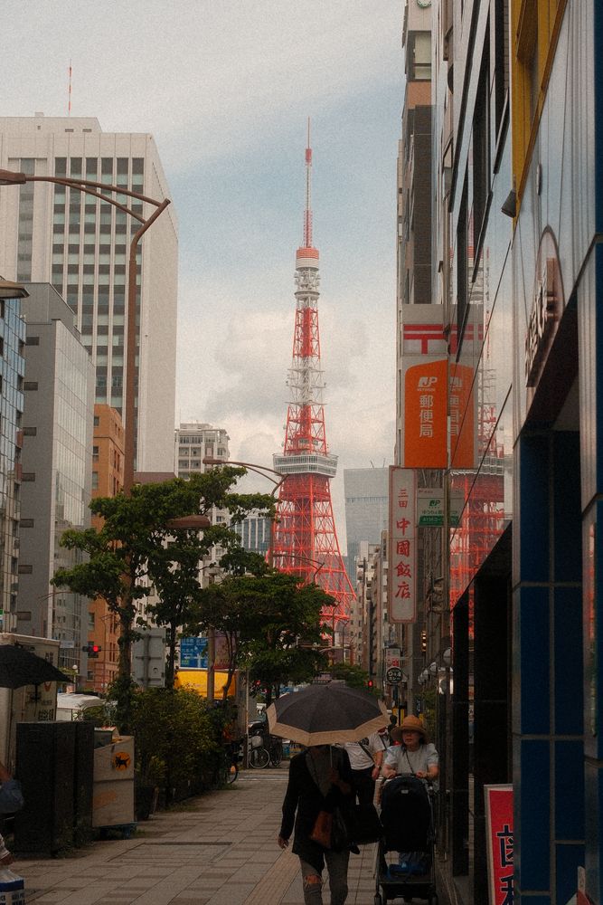 雨の街路。傘をさす人の奥に東京タワーが立つ